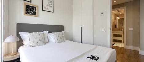 Un dormitorio ordenado con una cama grande, una mesita de noche con lámpara y citas motivacionales enmarcadas en la pared.