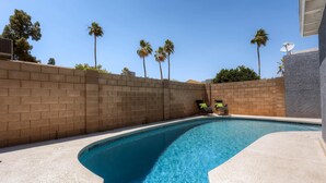 A swimming pool with a curved edge, surrounded by a brick wall and palm trees. - PX032 4 Bedroom Holiday home By Senstay (Scottsdale)