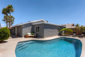 Ein modernes Haus mit Swimmingpool, einer Terrasse mit Liegestühlen und einem kleinen Garten.