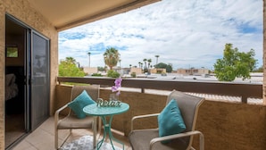 A balcony with two wicker chairs, a small round table, and a view of a residential area with palm trees and houses. - PX033 1 Bedroom Apartment By Senstay (Phoenix)