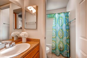 Un baño con lavamanos blanco, espejo y cortina de ducha con diseño geométrico.