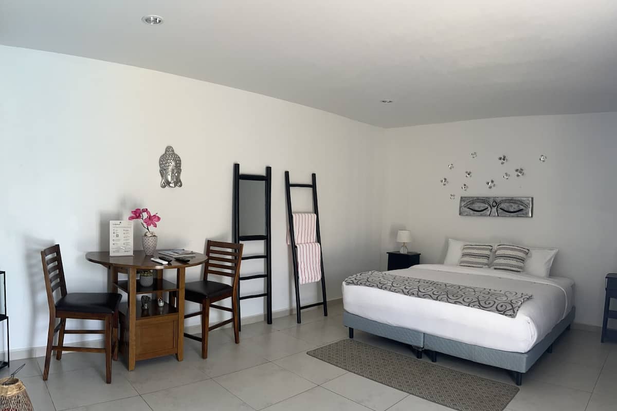 Un dormitorio con cama, mesita de noche, lámpara y una pequeña mesa con sillas.