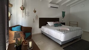 Un dormitorio con cama, mesita de noche, una silla, una pequeña mesa con una planta y un aire acondicionado instalado en la pared.