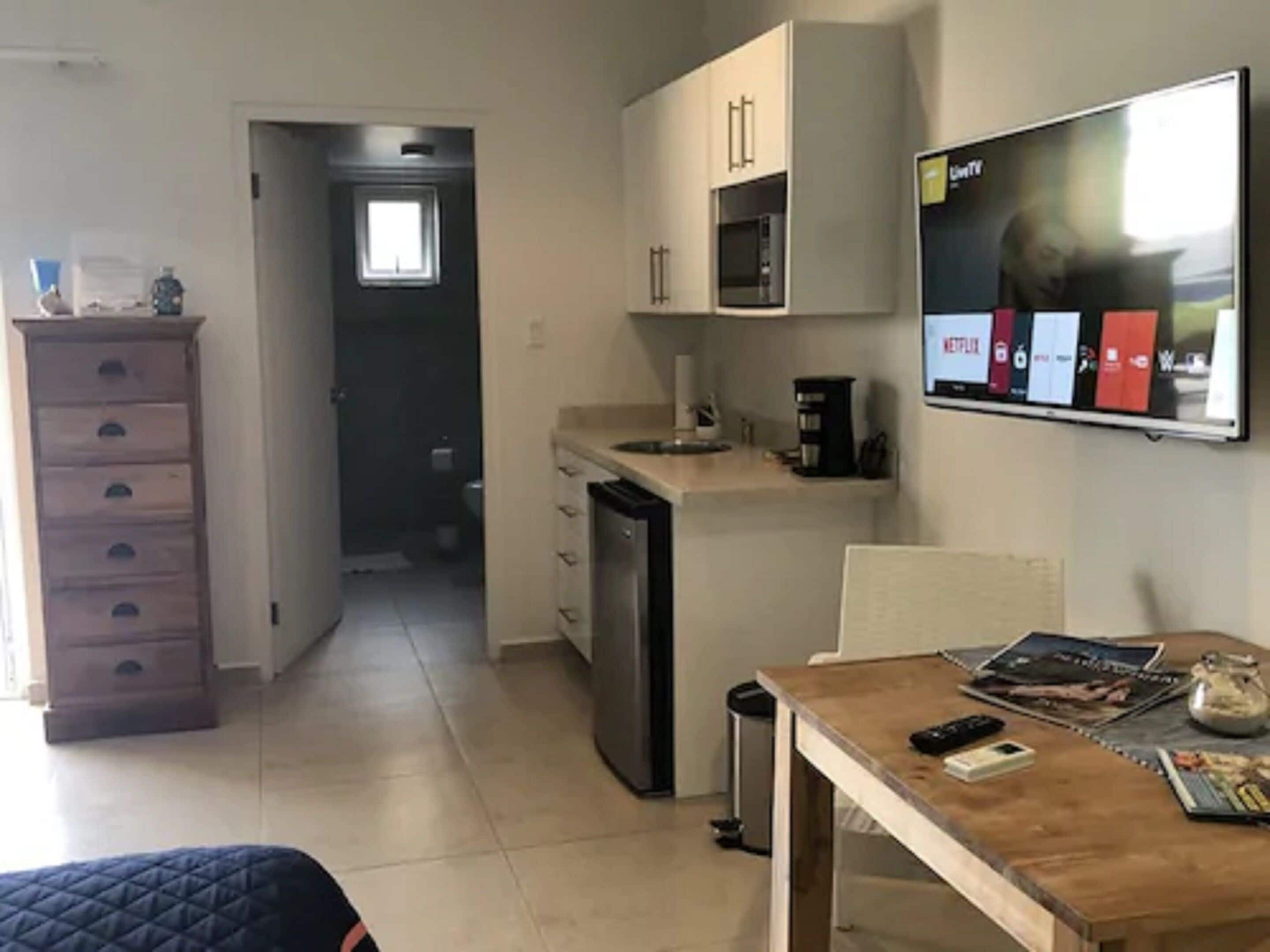 Eine kleine Küche mit Mikrowelle, Kaffeemaschine und einem Fernseher, der einen Streaming-Dienst anzeigt.