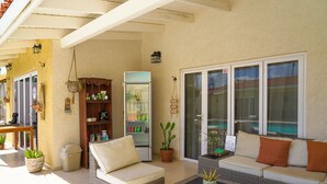 Un espacio exterior techado con mobiliario de mimbre, un refrigerador y plantas en macetas.