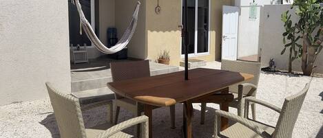 A patio with a wooden table and wicker chairs, a red umbrella, a hammock, and a cactus plant.