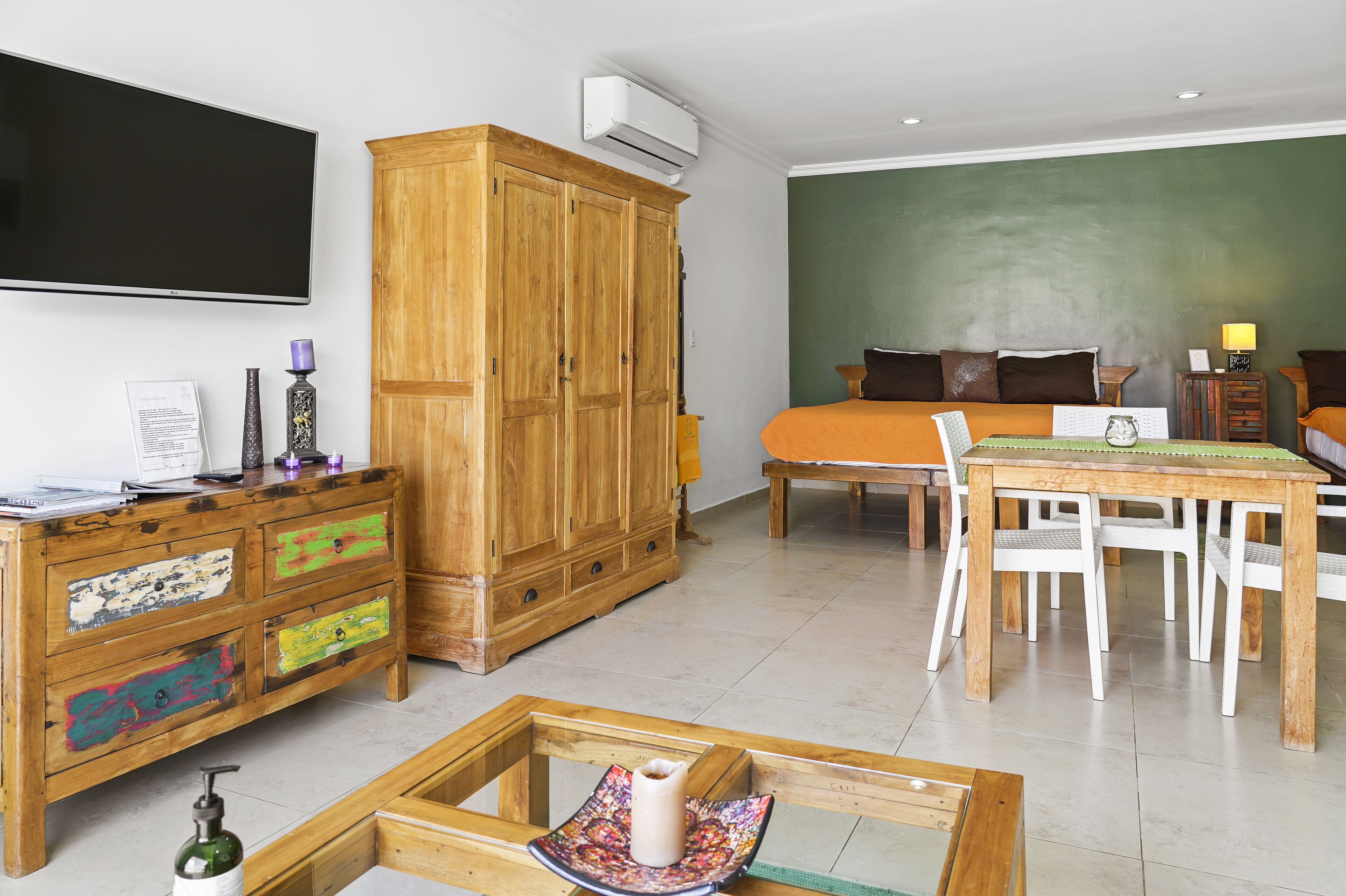 A bedroom with a bed, a wooden wardrobe, a desk with drawers, and a table with chairs.