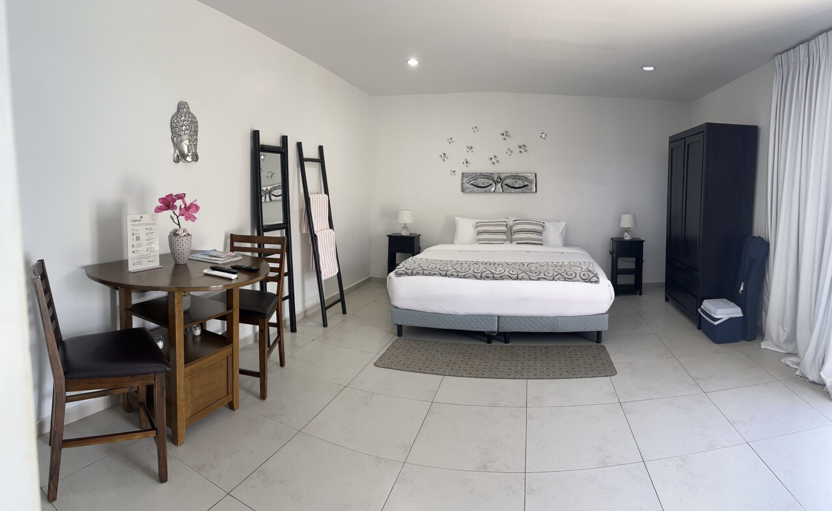 Une chambre d’hôtel comprenant un lit, un bureau avec des chaises, une petite table avec un vase de fleurs et une armoire.