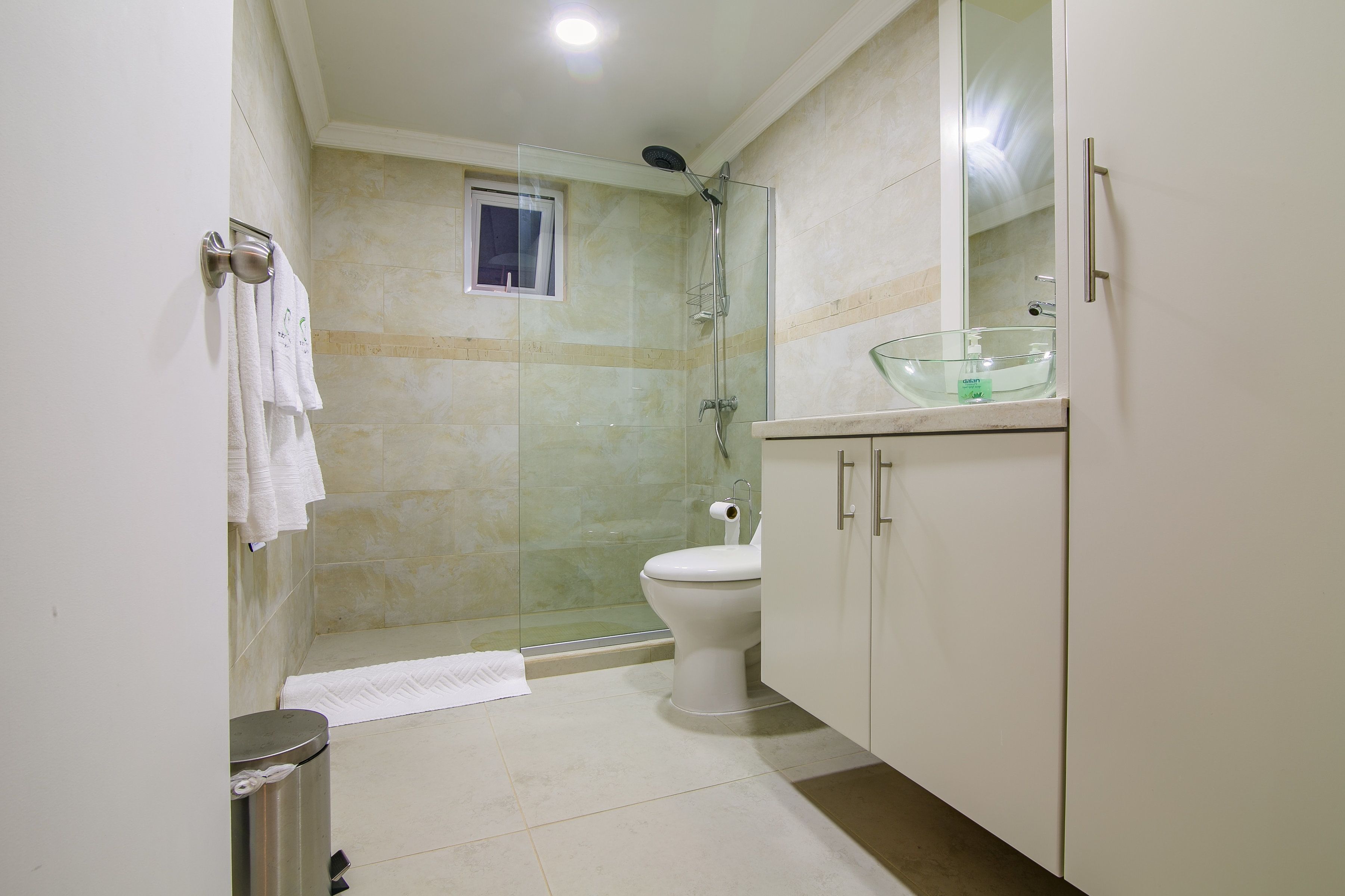 A bathroom with a glass-enclosed shower, a toilet, a sink with a glass basin, and a window.