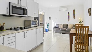 Una cocina moderna con armarios blancos, un microondas, una estufa y un refrigerador. Hay un comedor con una mesa y sillas de madera.