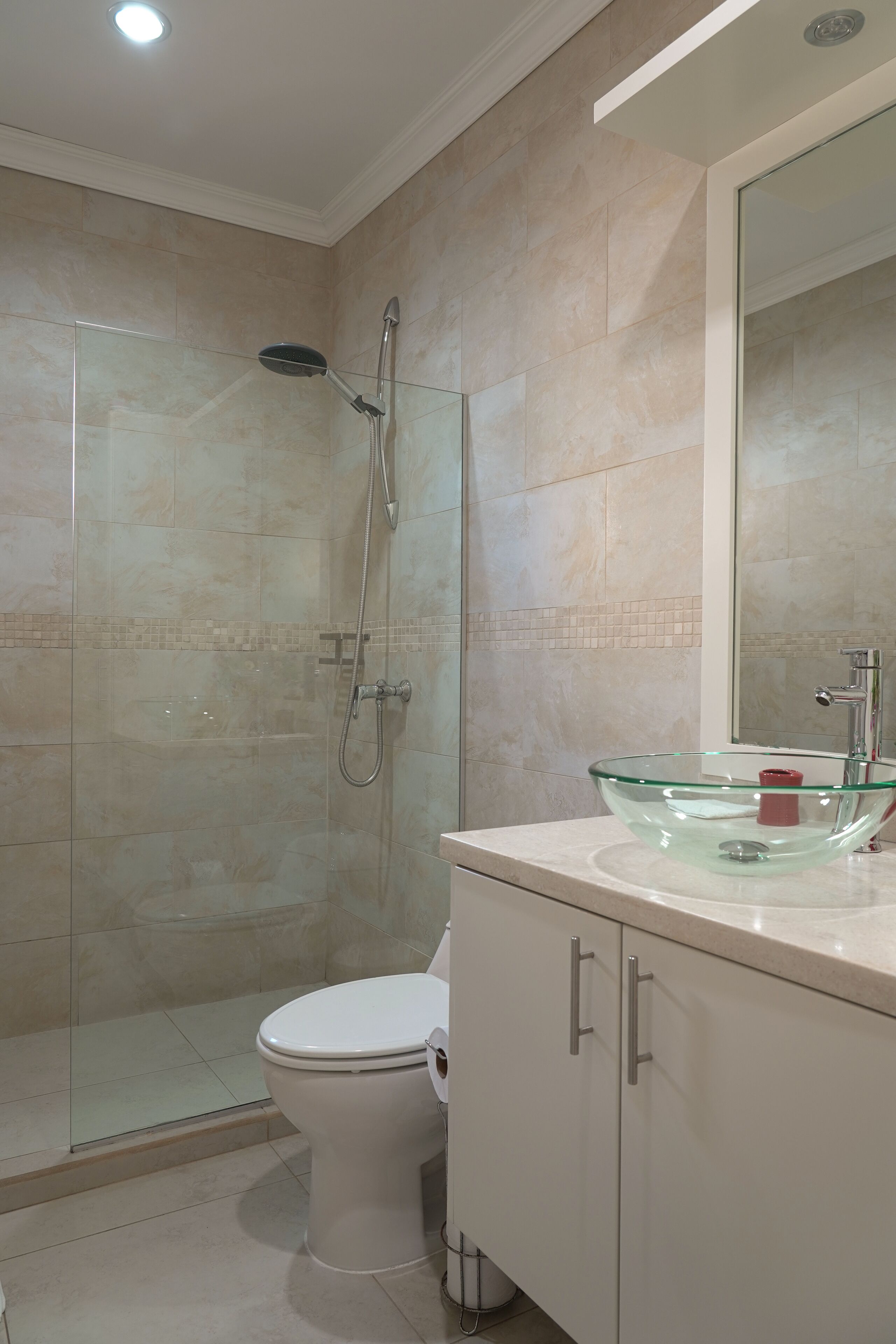 Un baño moderno con ducha de vidrio, inodoro blanco y lavamanos de vidrio.