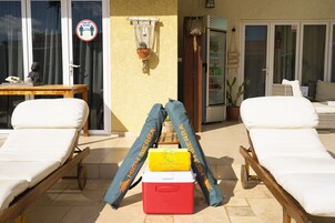 Un espacio al aire libre iluminado por el sol con dos sillones, un refrigerador y una nevera.