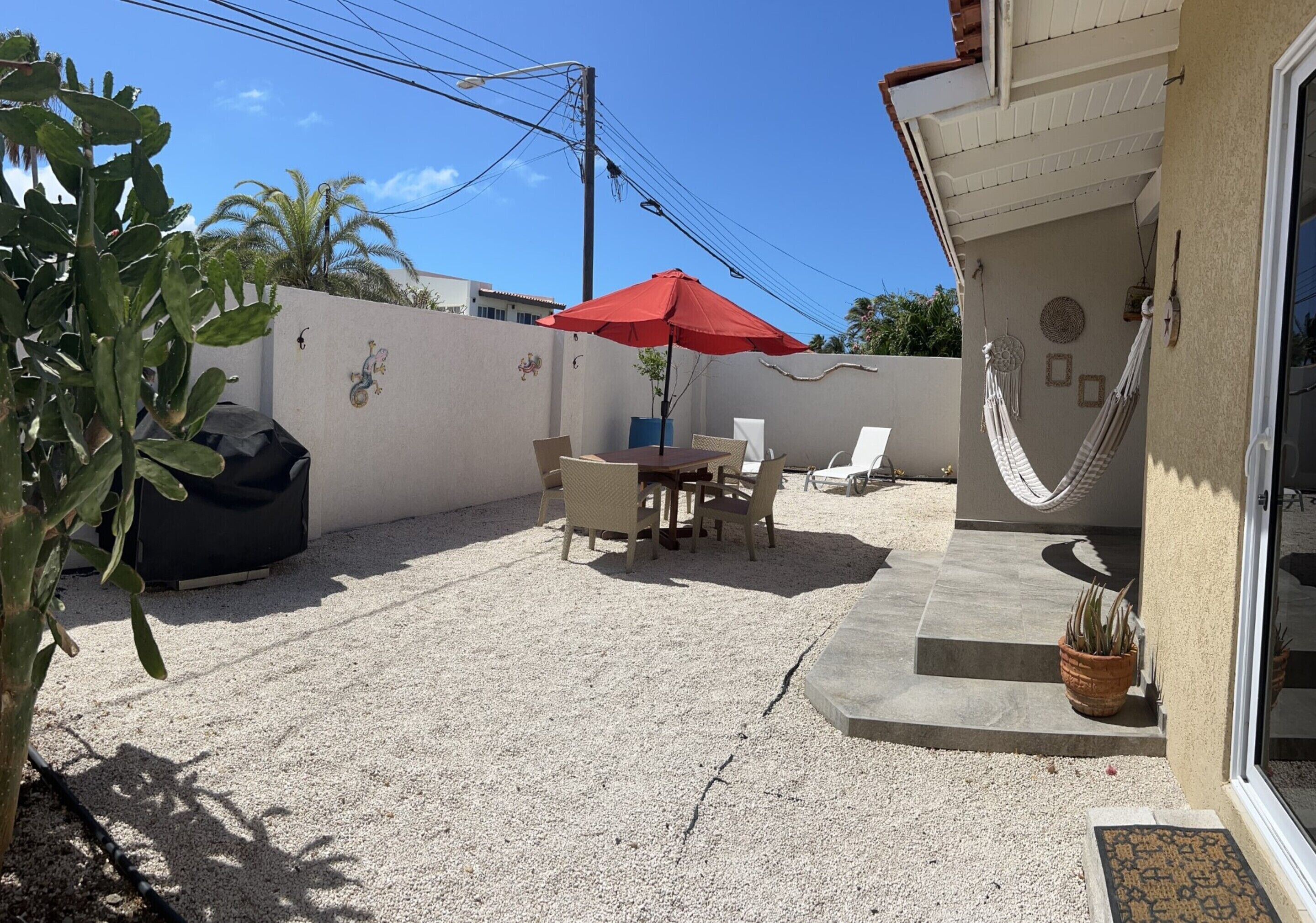 Une terrasse avec une table et des chaises, un parasol rouge, un hamac et une plante en pot.