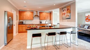 A modern kitchen with wooden cabinets, a stainless steel refrigerator, a microwave, and a large island with bar stools. - PX037 3 Bedroom Apartment By Senstay (Phoenix)