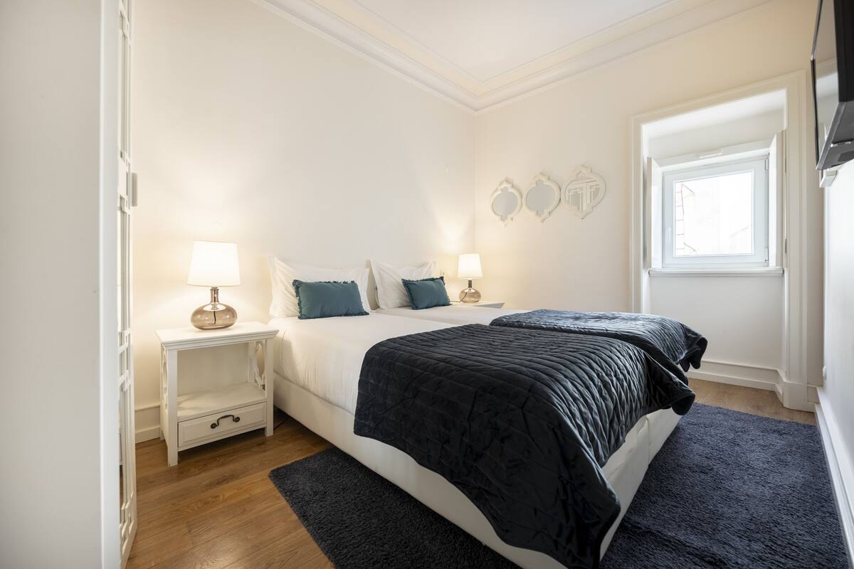 Une chambre avec deux lits, une table de chevet avec une lampe, une fenêtre et une porte.