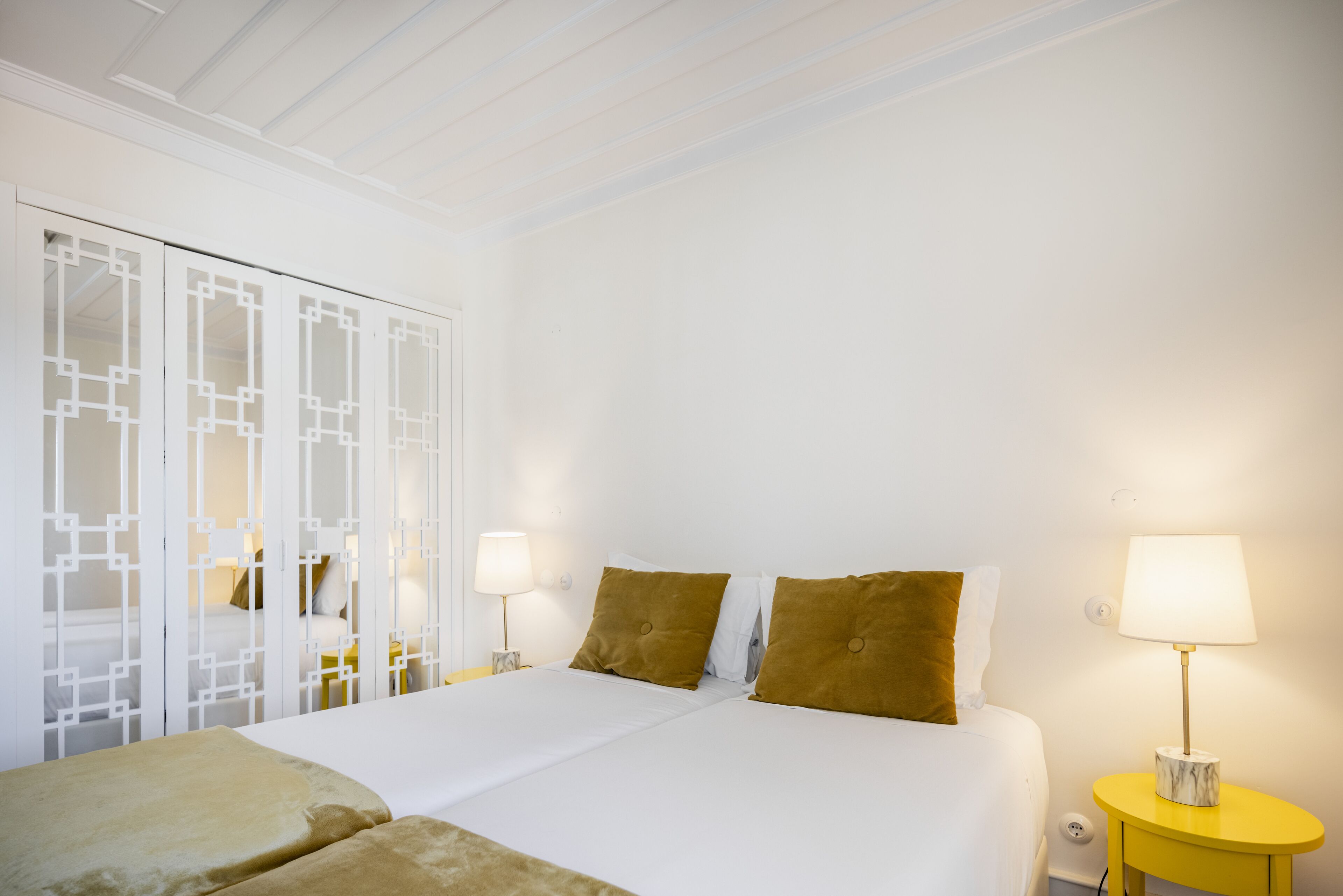 Une chambre d’hôtel comprenant un lit, deux tables de chevet, une petite table et une porte coulissante ornée d’un motif géométrique.