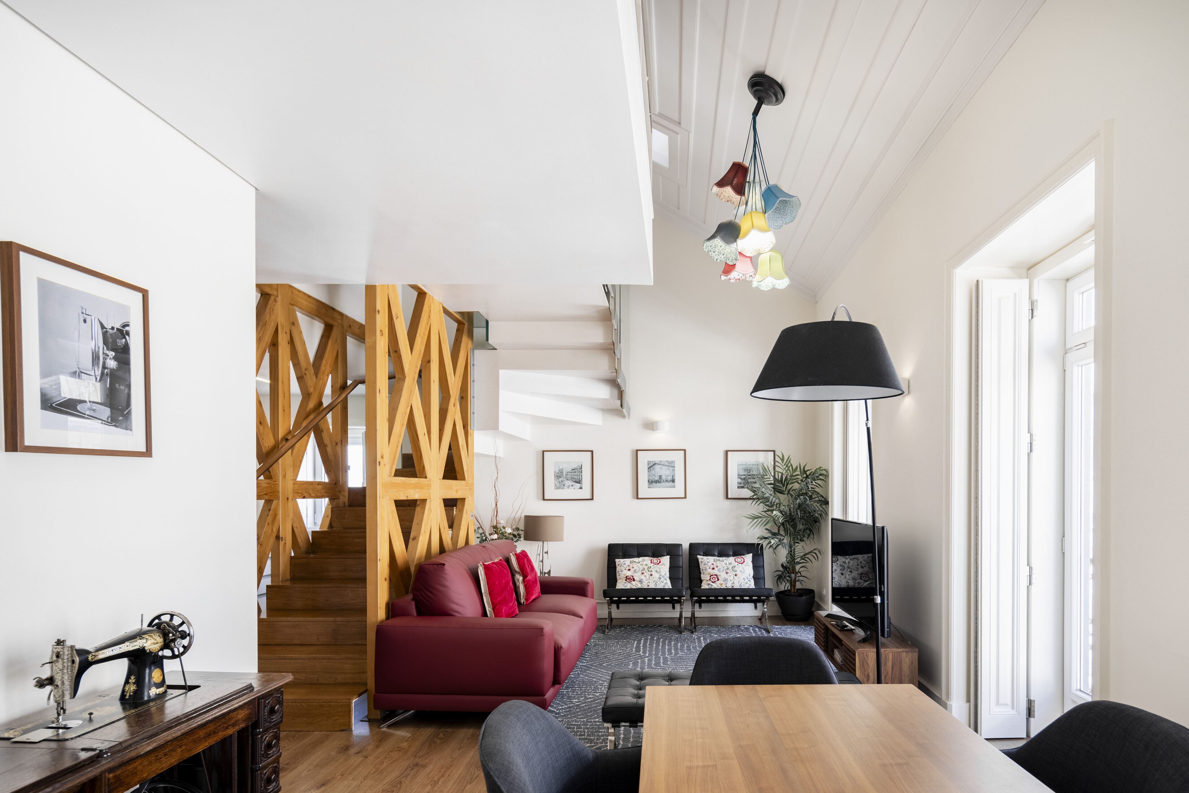 A modern living room with a staircase, a red sofa, a wooden dining table, and a TV.