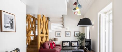 A modern living room with a staircase, a red sofa, a wooden dining table, and a TV.