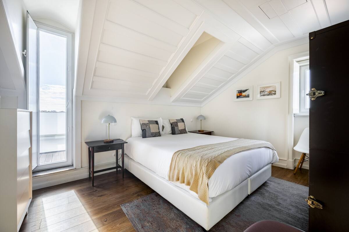Une chambre à coucher avec un grand lit, une table de chevet, un bureau, une chaise et une fenêtre donnant sur un beau paysage.