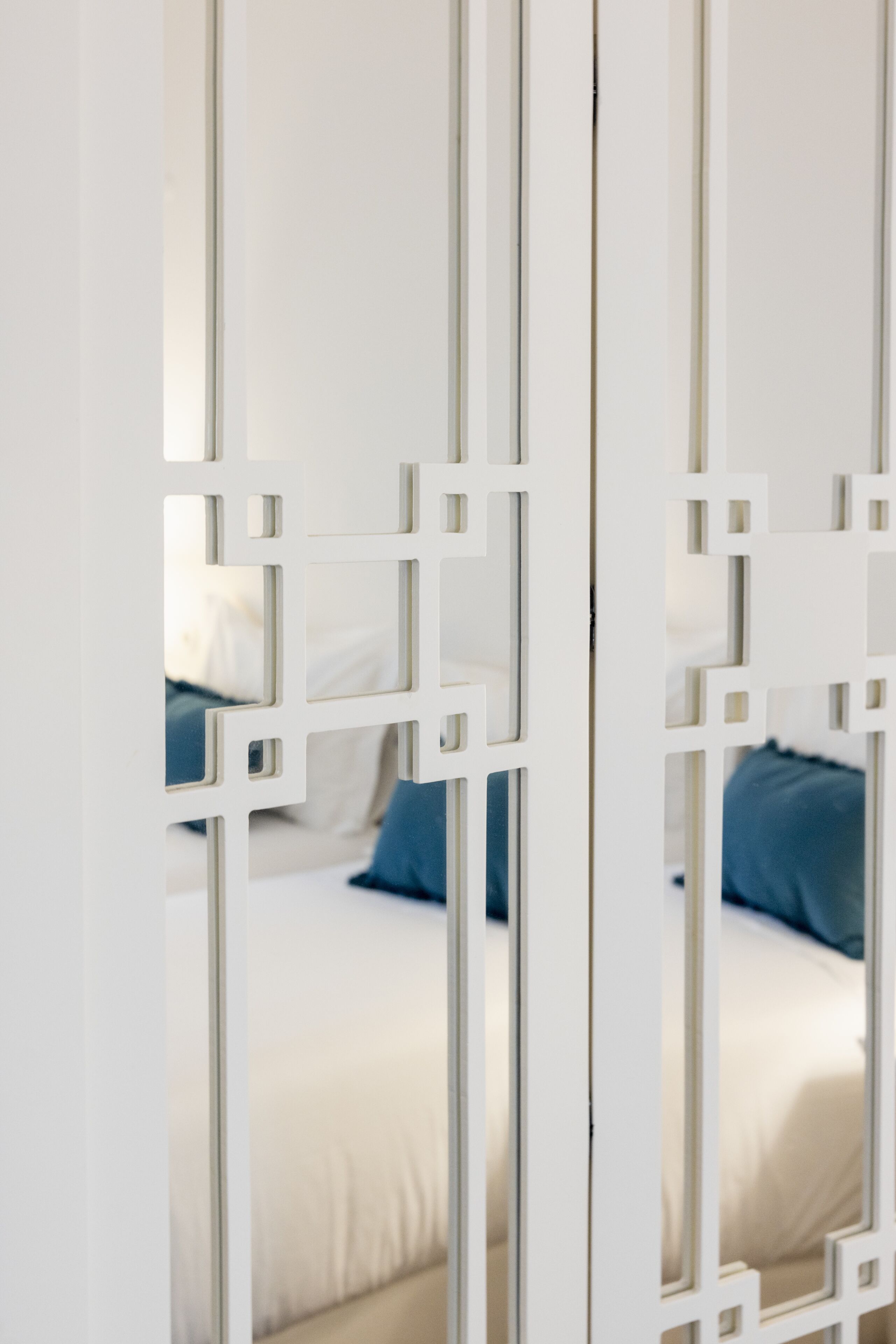 Een witte scheidingswand met een geometrisch patroon, een bed met een blauw kussen en een wit hoofdeinde.
