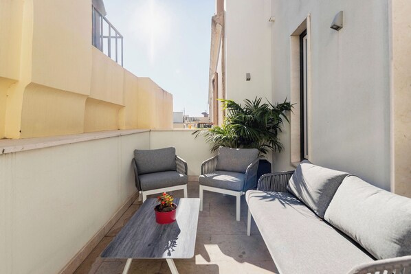 Un petit espace extérieur aménagé avec un canapé, deux chaises et une table sur laquelle est posée une plante en pot.