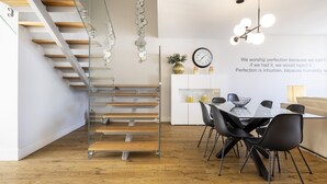 A modern kitchen with a glass staircase, wooden flooring, and a dining area with black chairs and a white table. - Chiado Square - Lisbon Best Apartments (Lisbon)