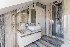 Une salle de bain moderne avec un mur en marbre, un lavabo blanc et une cabine de douche en verre.