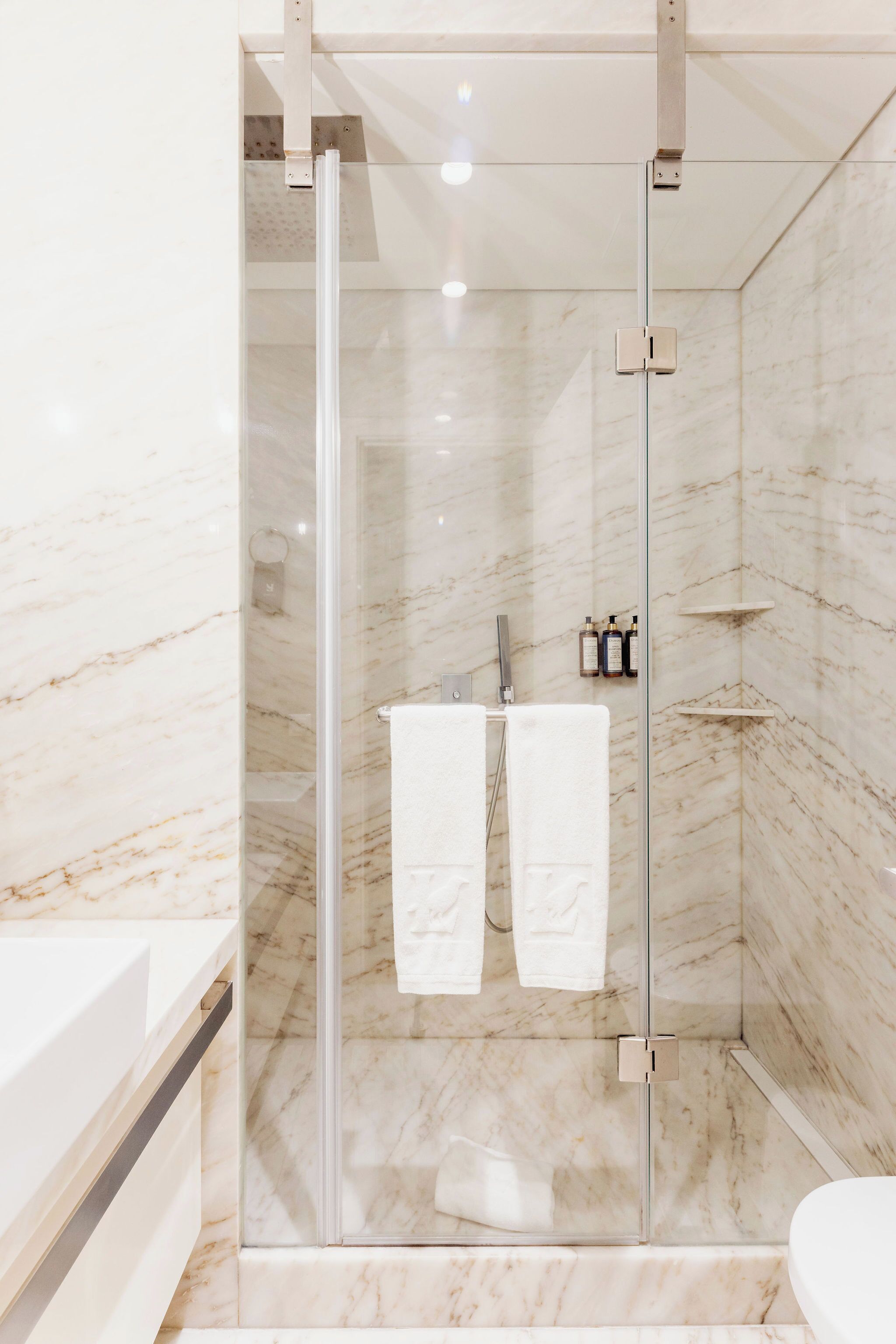 Een moderne badkamer met een douche met glazen wanden, marmeren wanden en een witte wastafel.