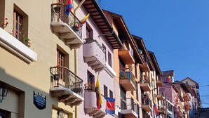 A row of traditional European-style buildings with balconies, a cobblestone street, and flags. - Hotel Casa Ecuatreasures Centro Histórico (Quito)