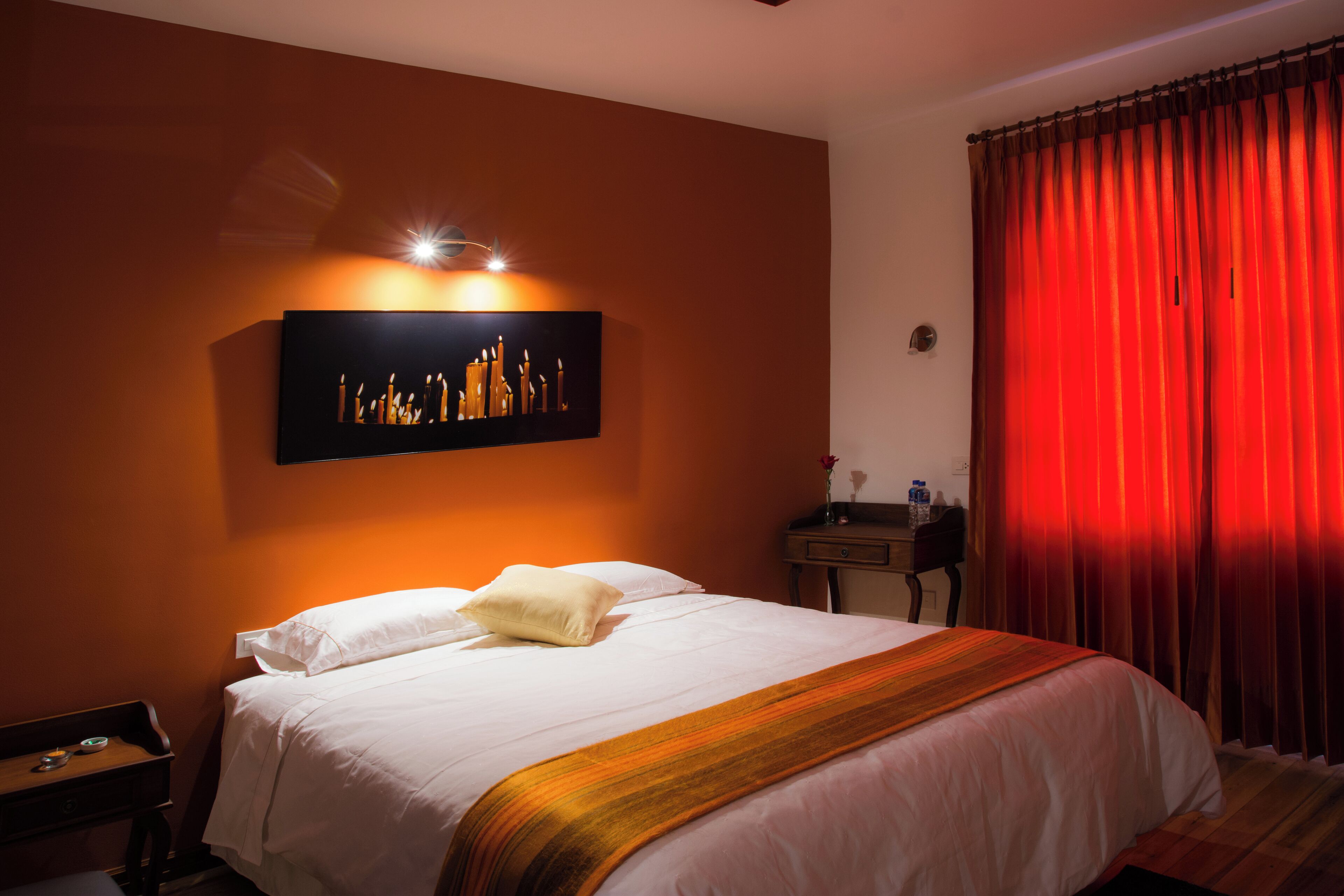 Ein Hotelzimmer mit Bett, Nachttisch, Wandleuchte und einem roten Vorhang.