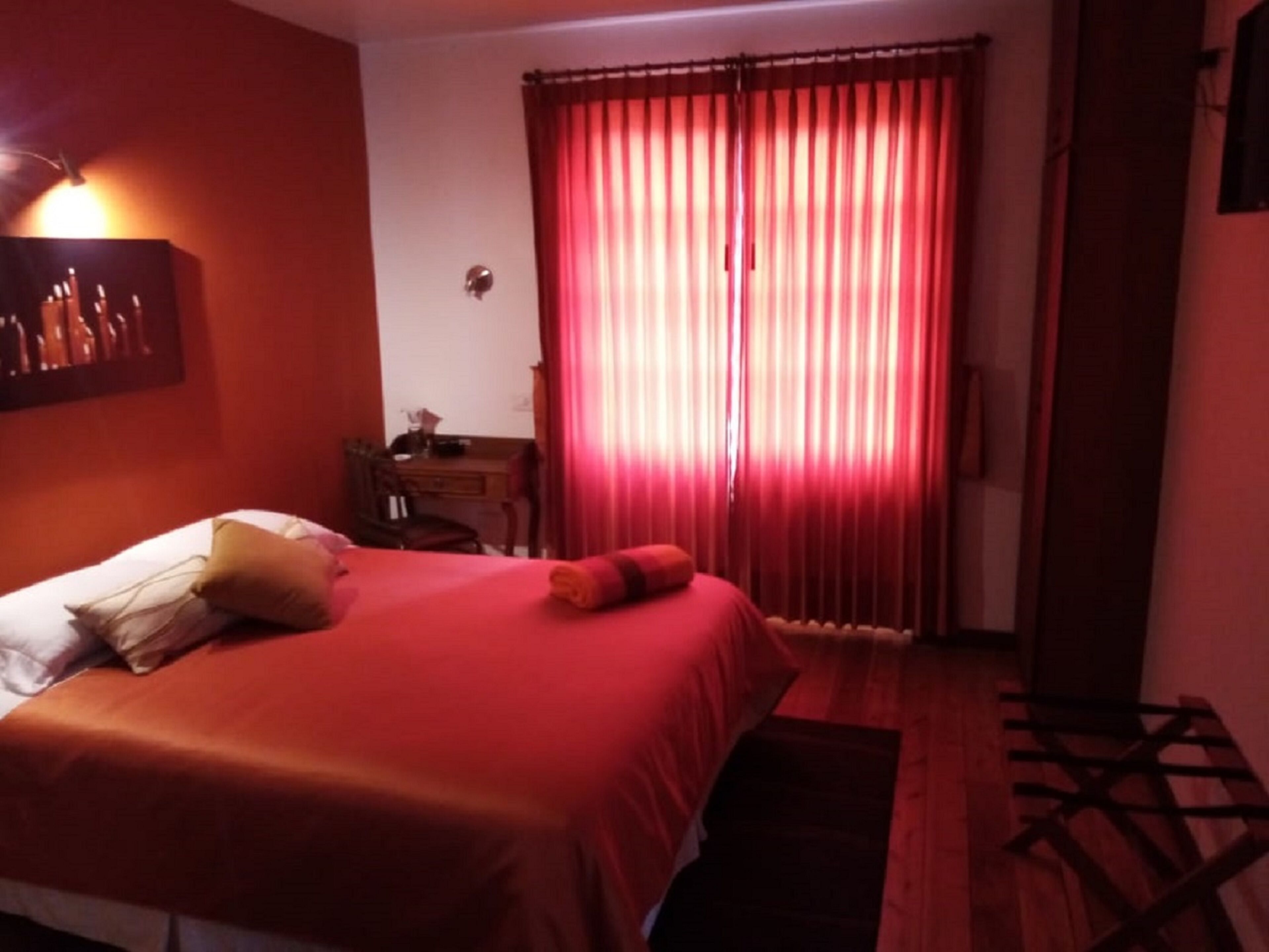 Una camera d'albergo con un letto, una scrivania e una finestra con tende rosse.