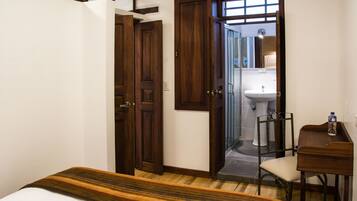 Een hotelkamer met een bed, een bureau, een stoel en een badkamer die door een open deur zichtbaar is.
