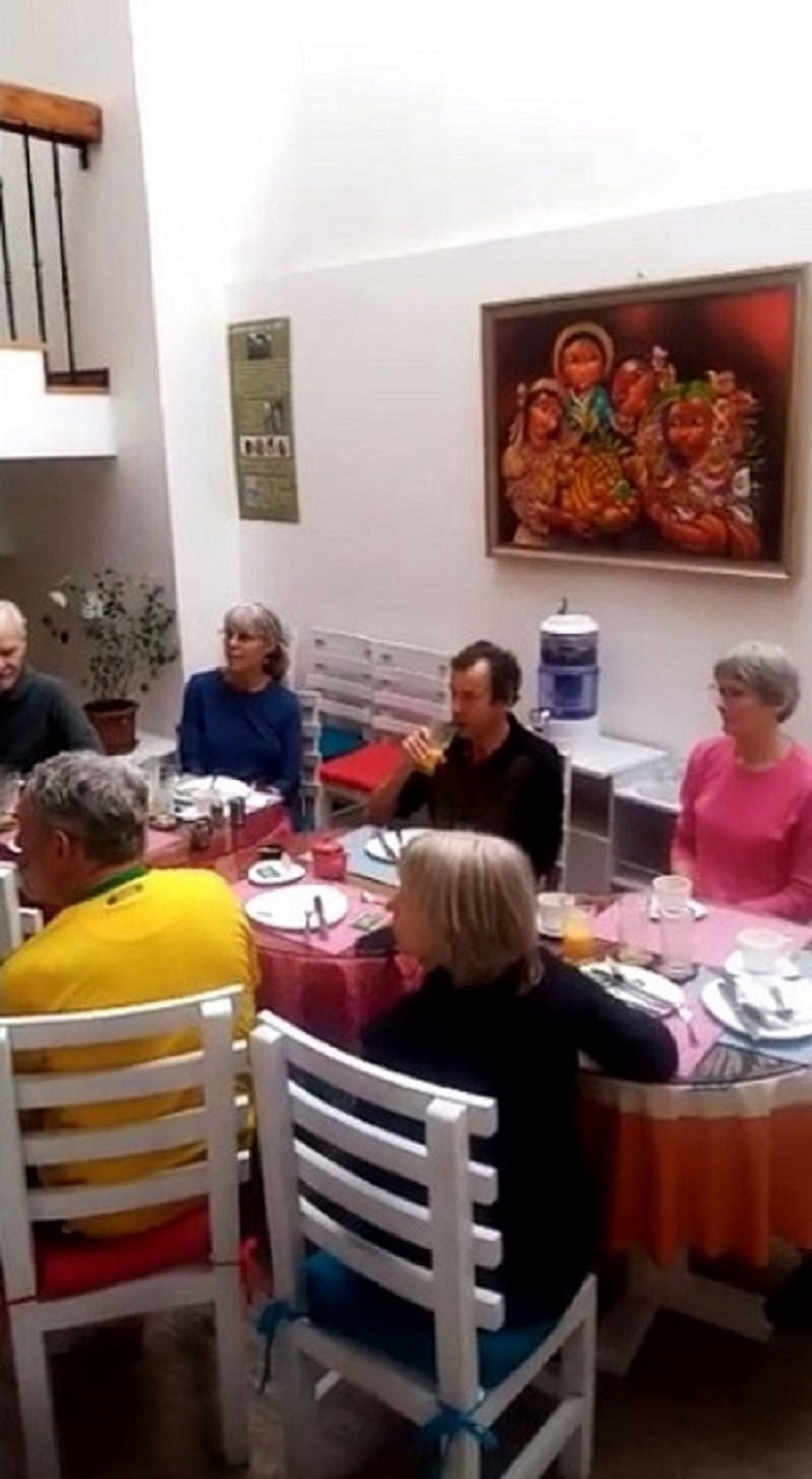 A group of people seated around a table in a dining area with a painting on the wall.