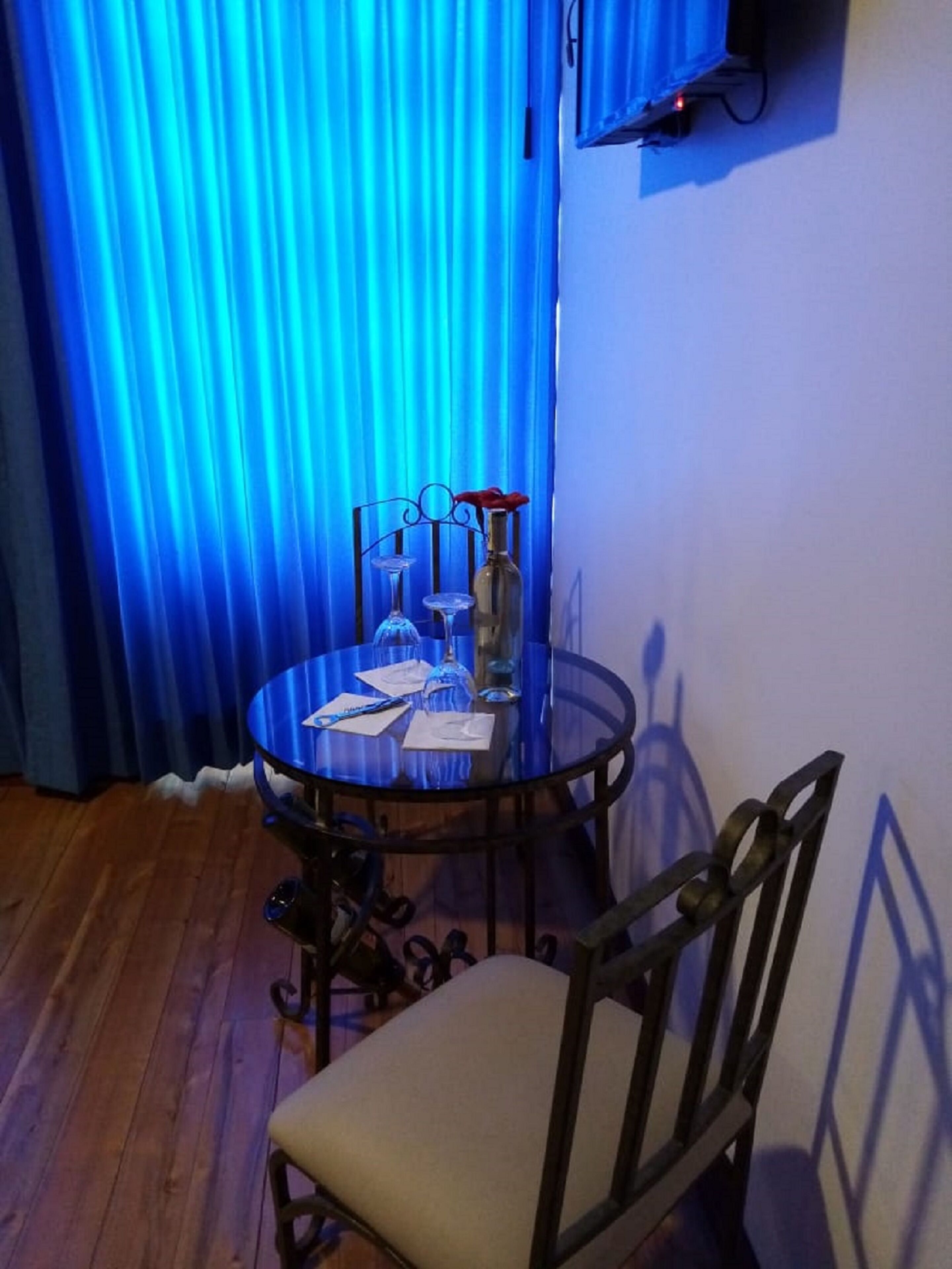 Uma mesa de vidro redonda com uma cadeira, uma garrafa e um vaso com uma flor vermelha.