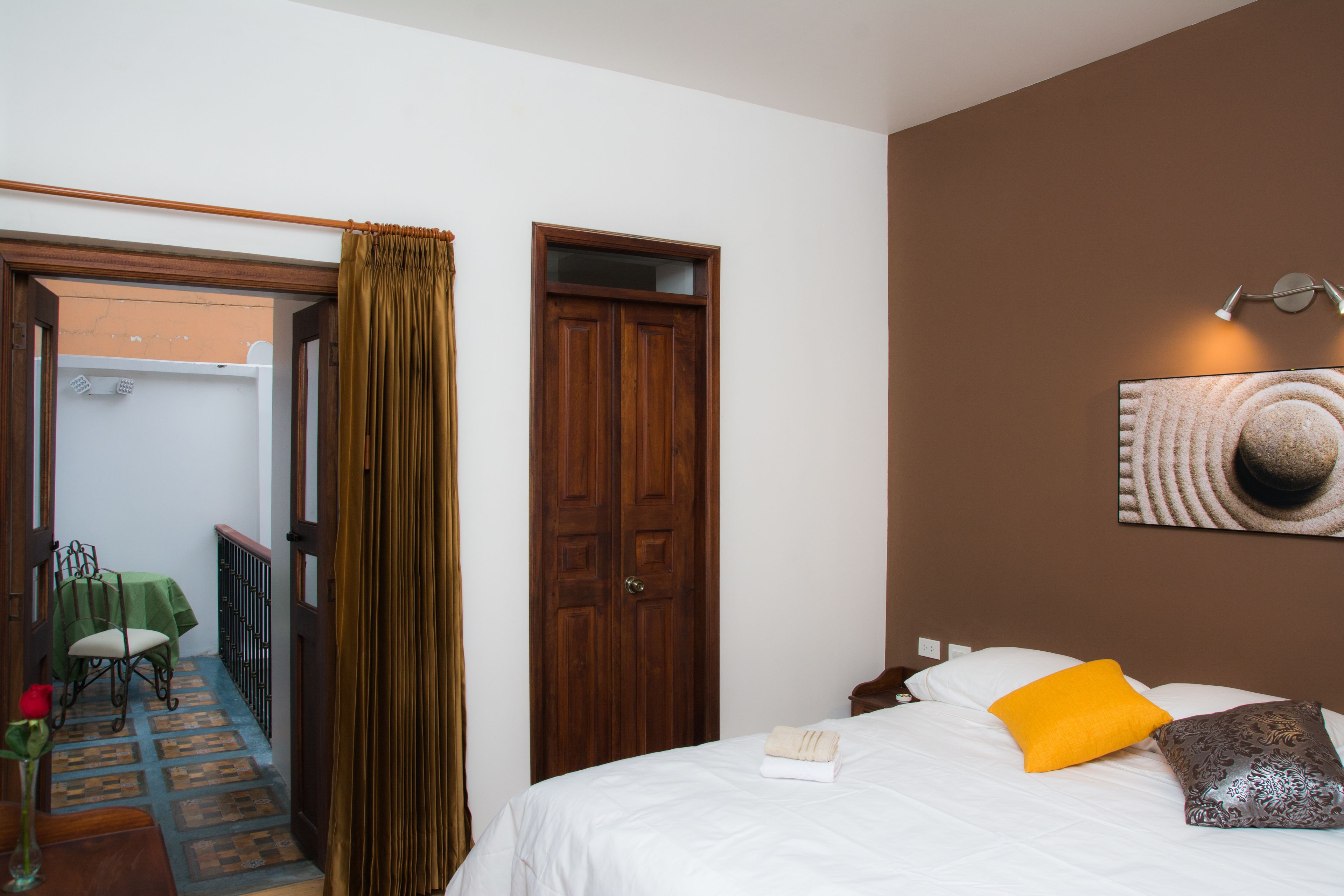 Habitació d'hotel amb un llit, una porta de fusta, una taula verda amb una cadira, i vista a l'exterior.