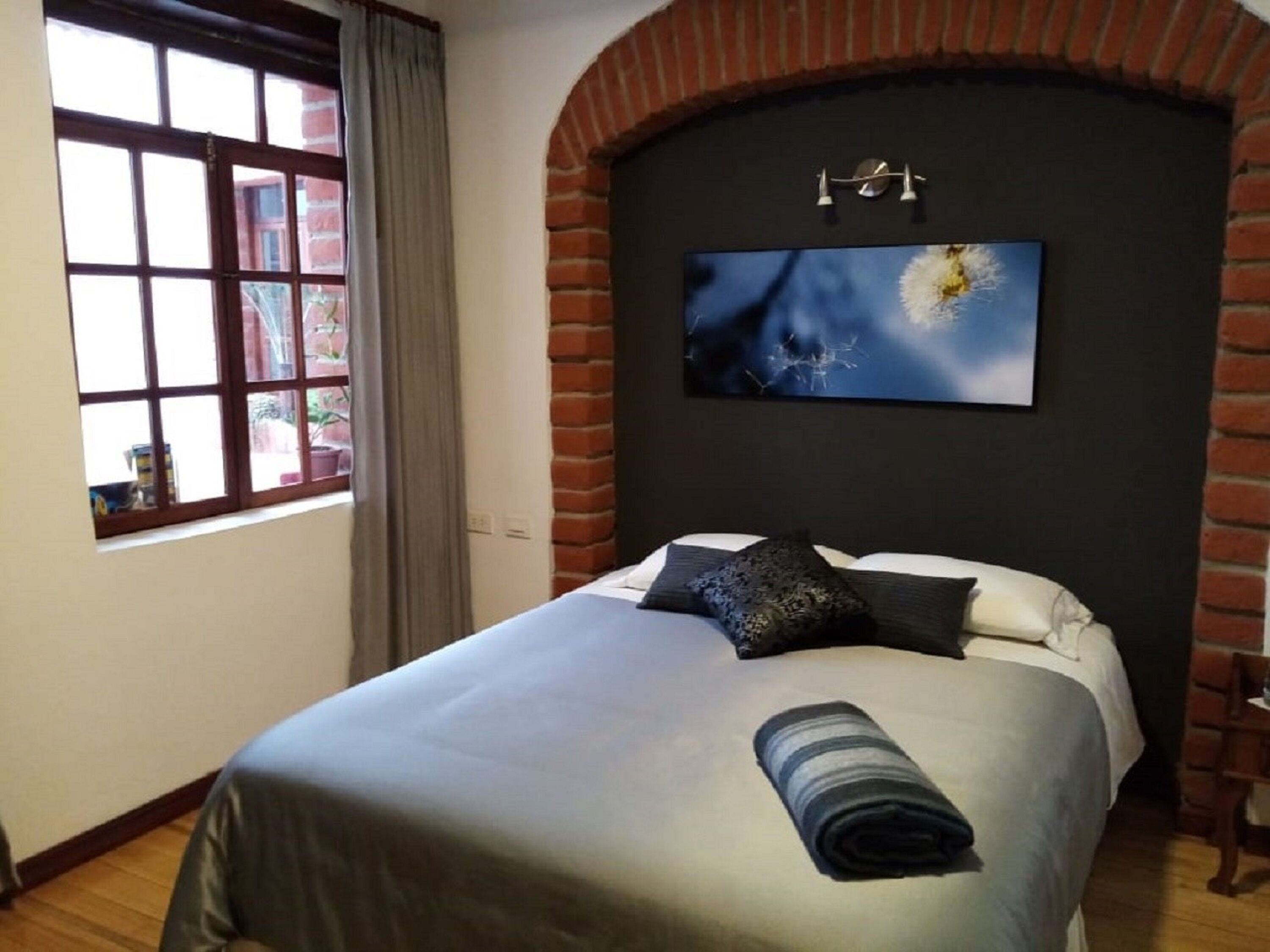 A bedroom with a large window, a brick fireplace, and a painting of a dandelion on the wall.
