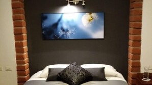 A bedroom with a brick arch, a bed with a grey bedspread, a black pillow, and a wall-mounted TV. - Hotel Casa Ecuatreasures Centro Histórico (Quito)
