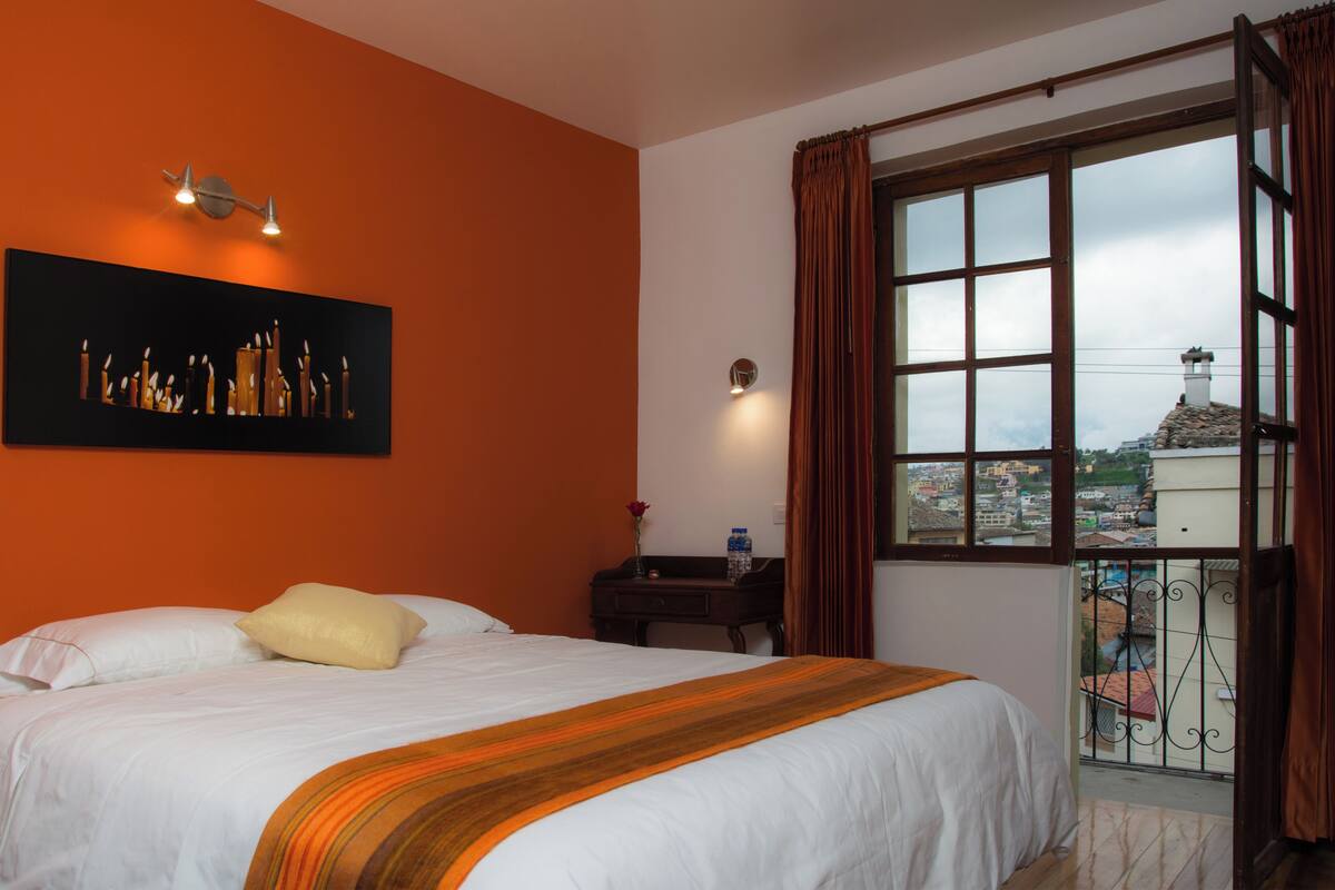 Ein Hotelzimmer mit einem großen Bett, einem Gemälde an der Wand, einem Fenster mit Vorhängen und Blick auf die Stadt.