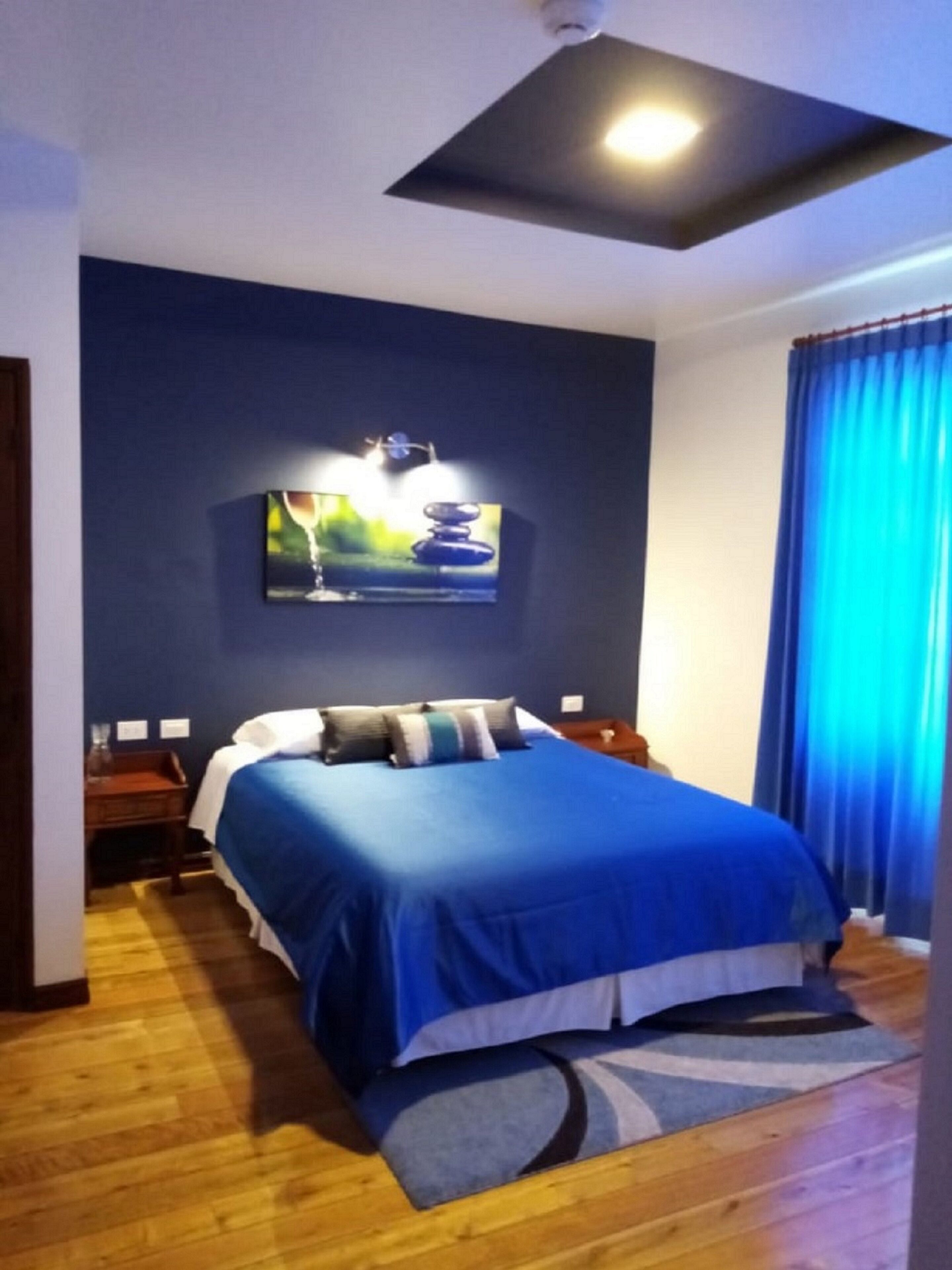 Un dormitorio con cama, mesita de noche, televisor de pared y luz de techo.