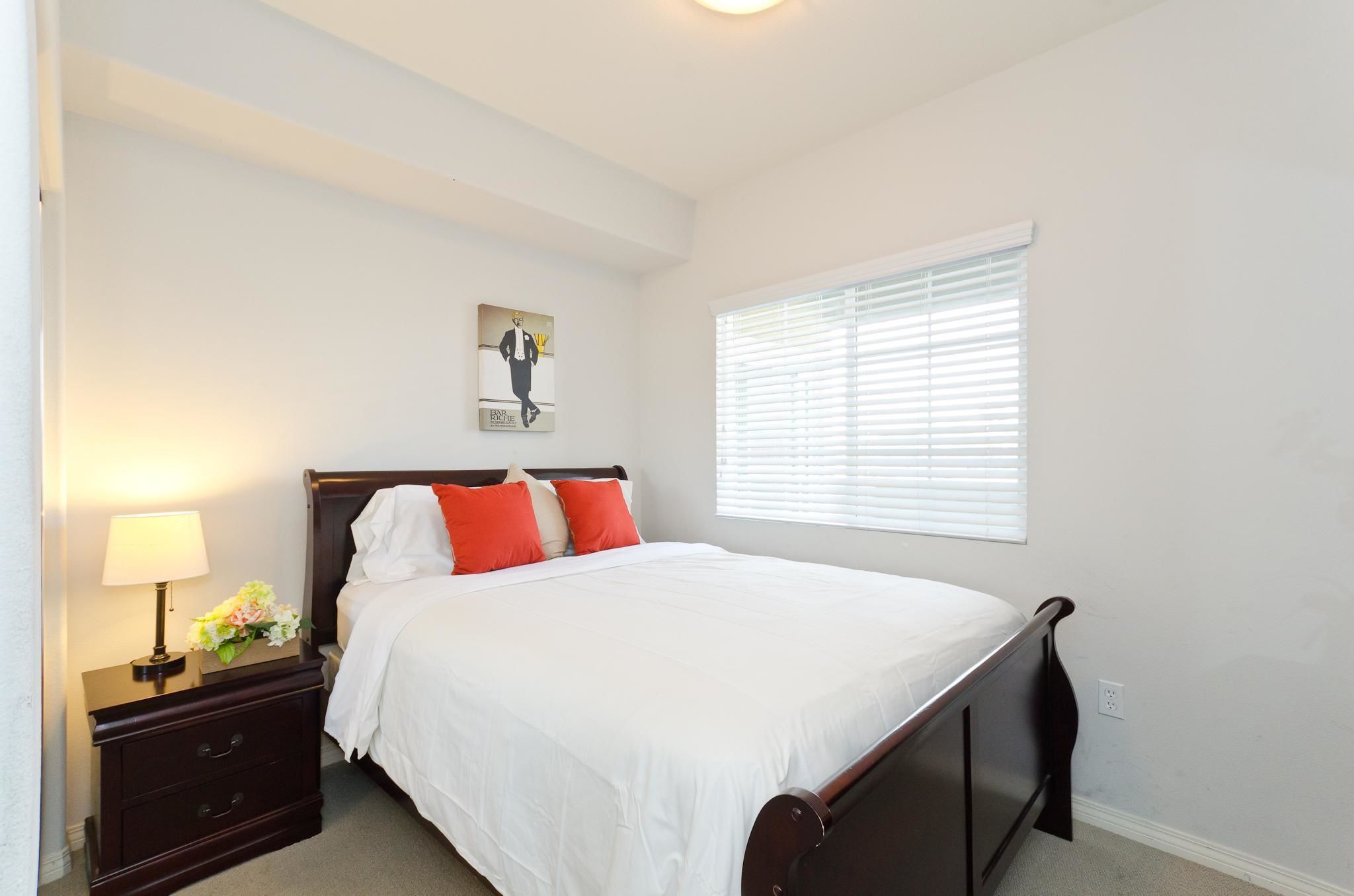 A neatly arranged bedroom with a single bed, a nightstand with a lamp, and a window with blinds.