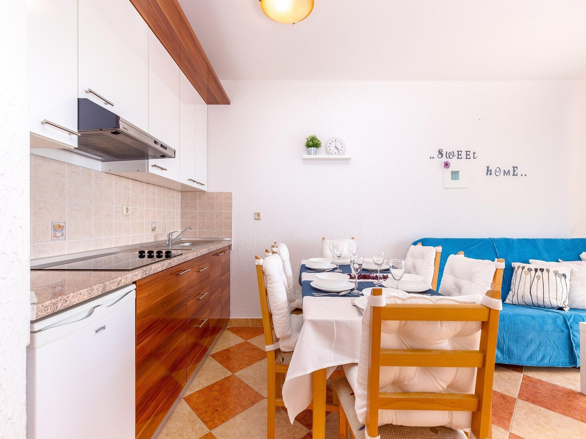 Cozinha moderna com armários brancos, forno embutido e área de jantar com sofá azul e cadeiras brancas.