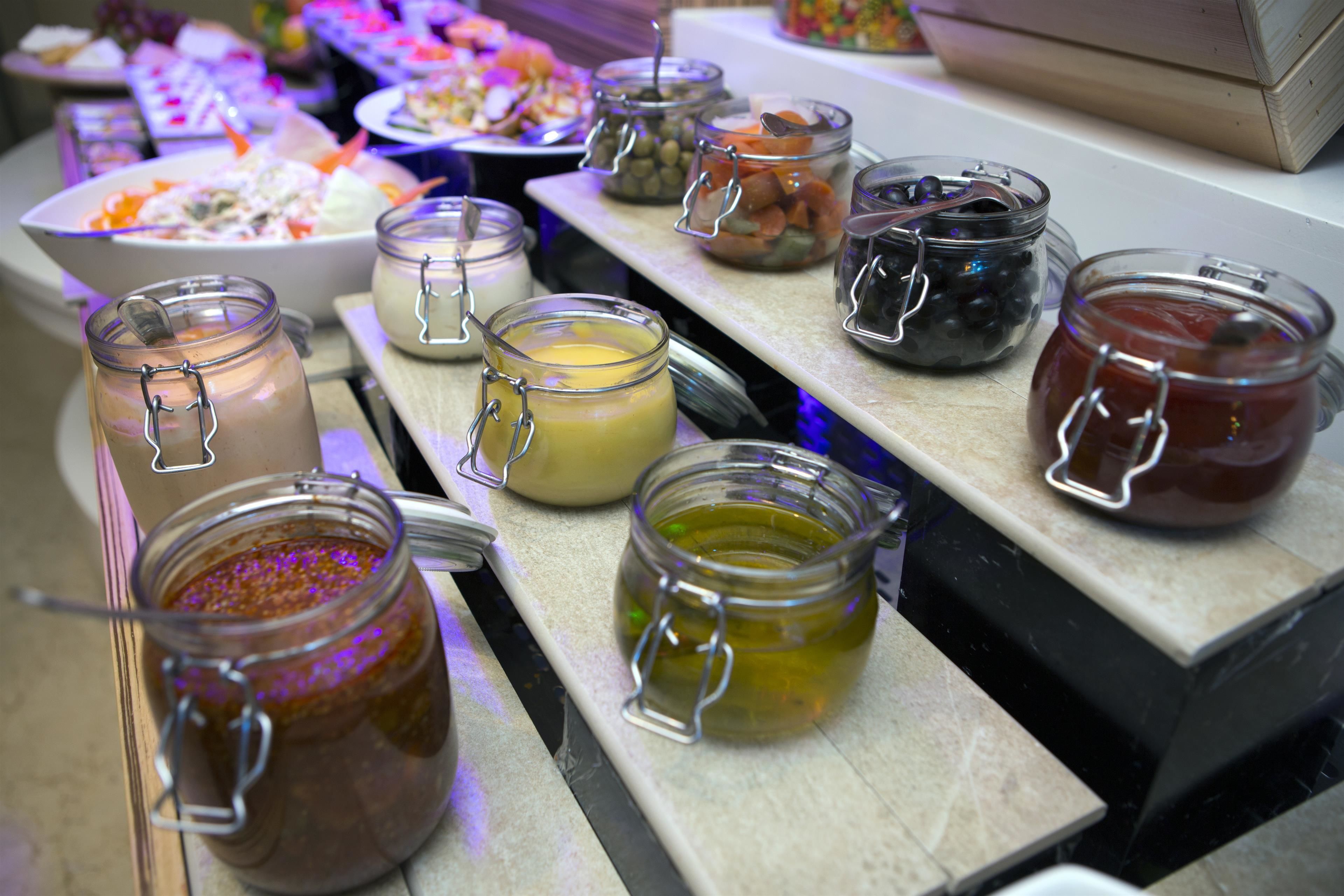 Uma mesa de buffet com diversos alimentos e acompanhamentos em potes de vidro.