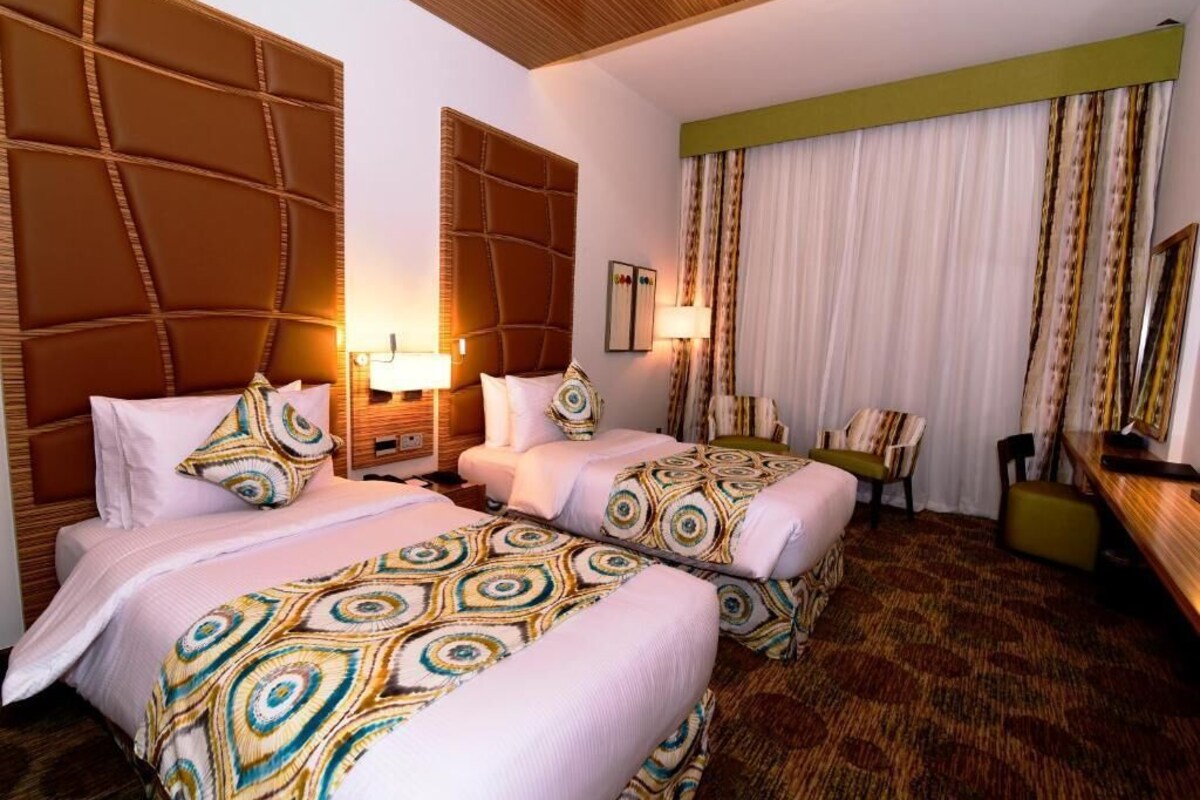 A hotel room with two beds, a large headboard, a desk, and a chair.
