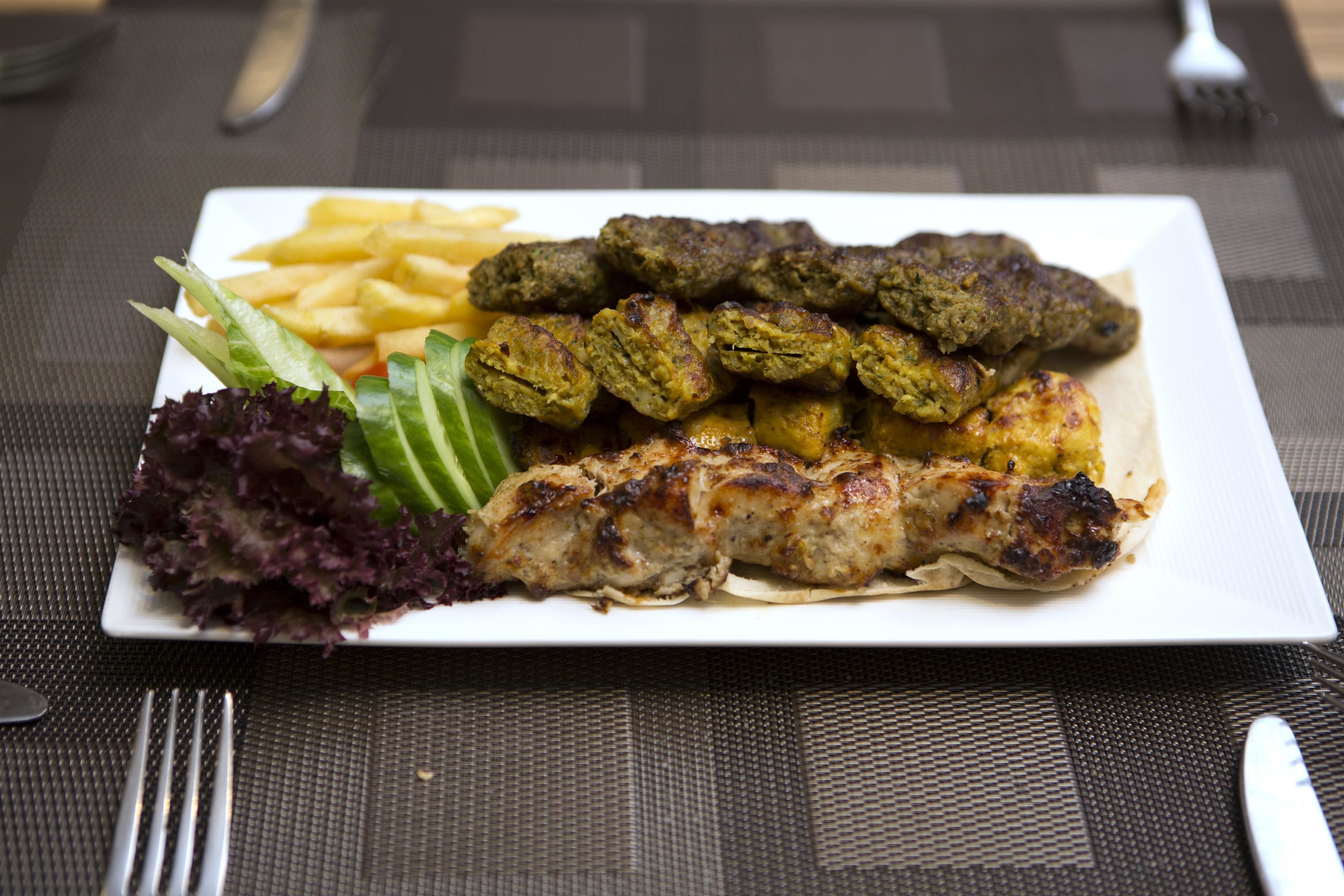 Une assiette de nourriture comprenant des brochettes, des frites et une salade, posée sur une table.