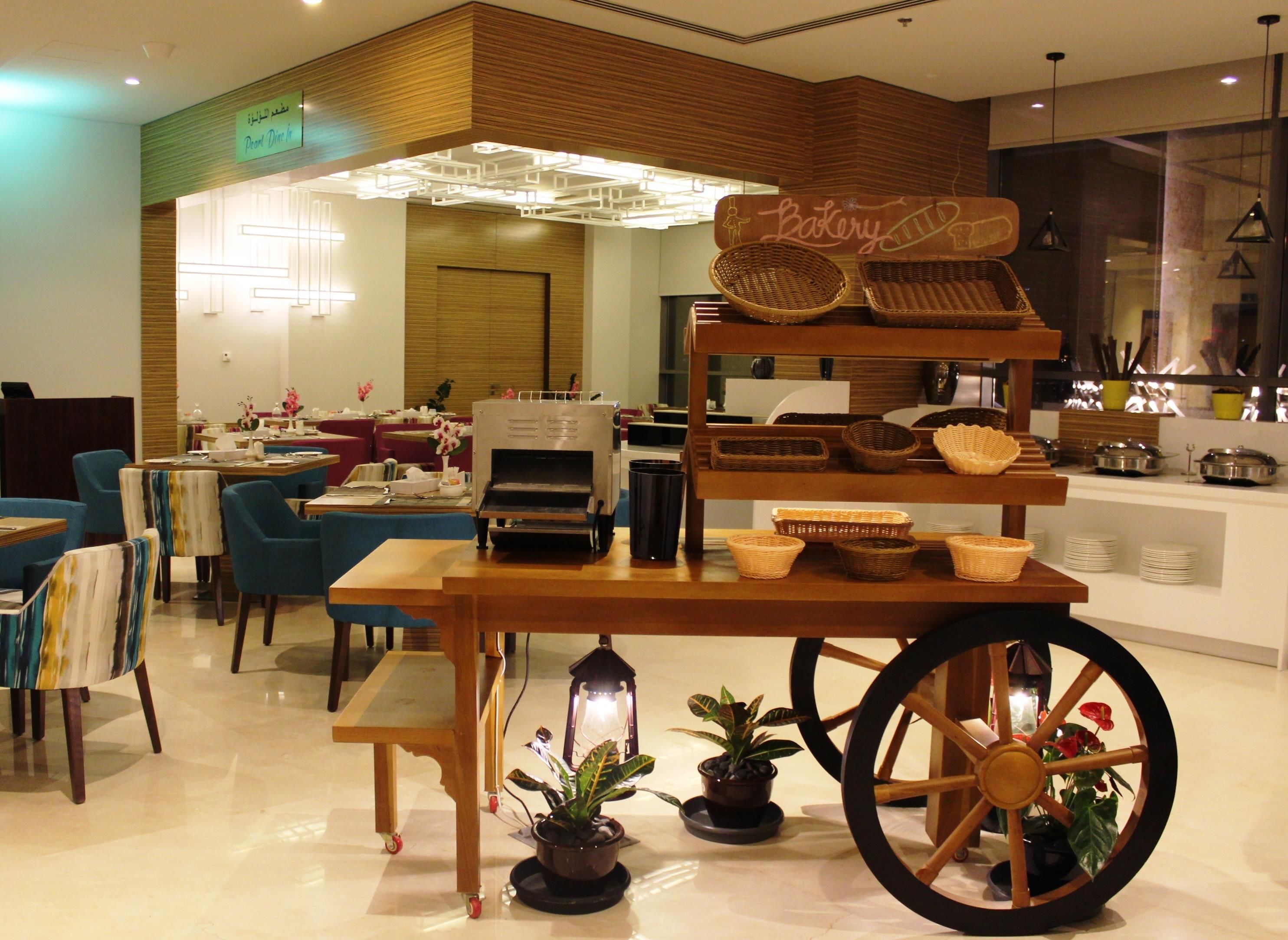 A bakery display with baskets and a sign, a coffee machine, and a cart with a plant.