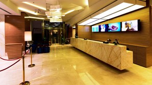 Un área de recepción de hotel moderna con un mostrador de mármol, una barrera de cuerda roja y un televisor de pantalla plana mostrando imágenes.