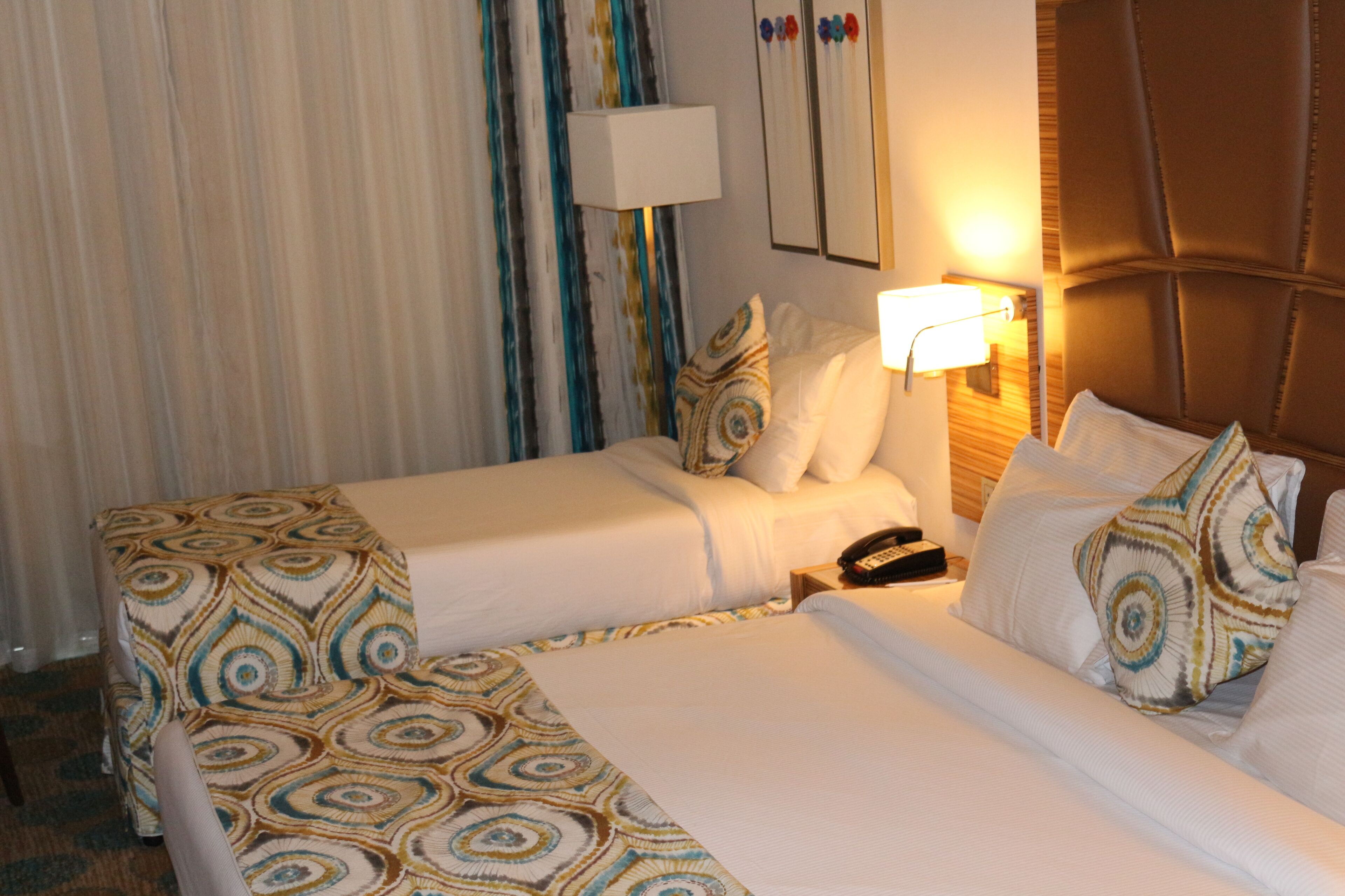 A hotel room with two beds, a bedside table with a lamp, and a telephone.