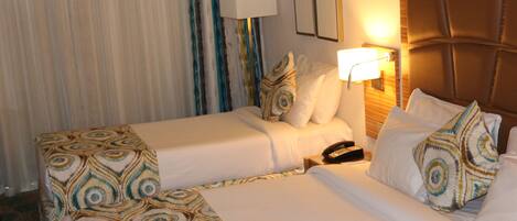 A hotel room with two beds, a bedside table with a lamp, and a telephone.