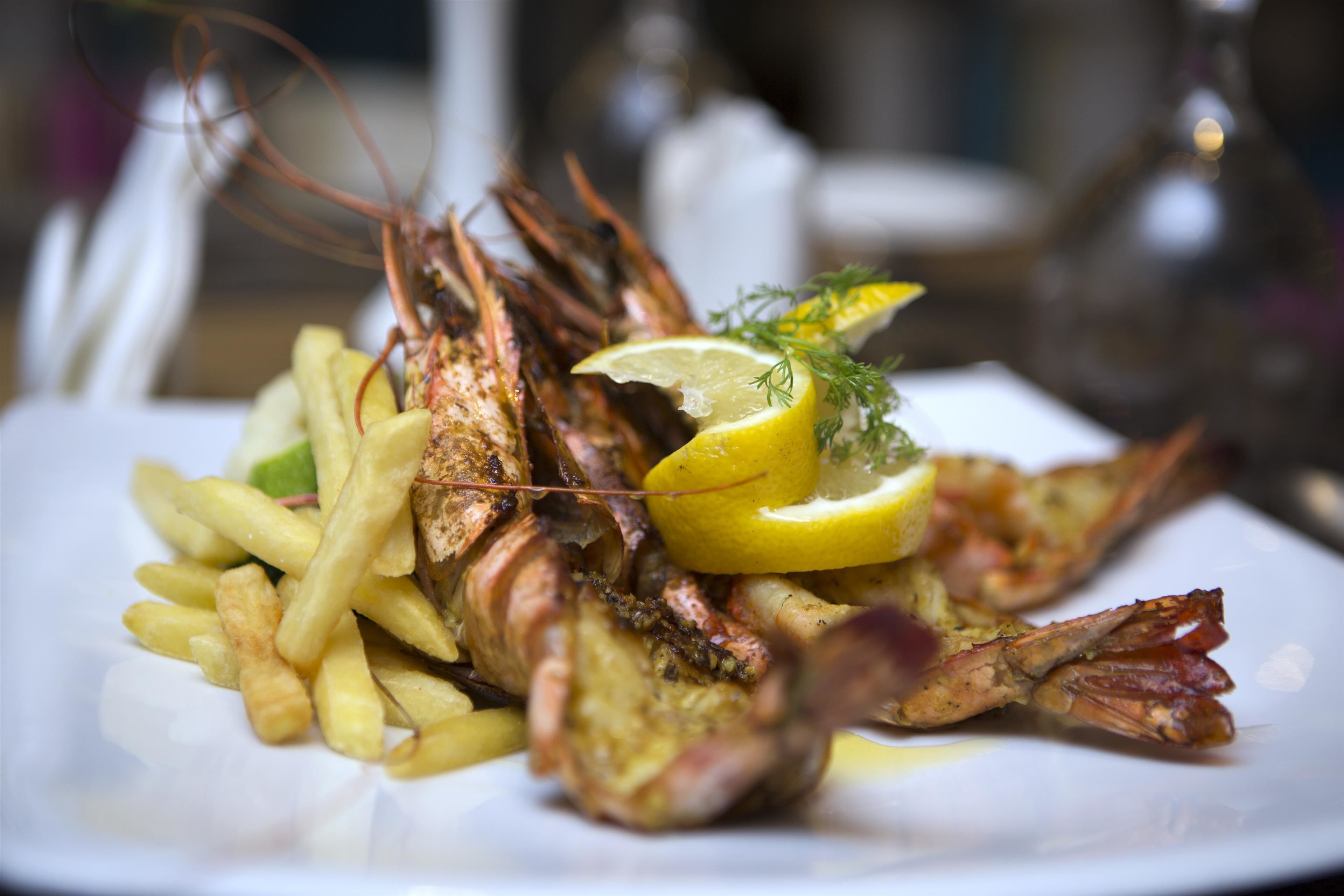 Prato com lagosta grelhada, fatias de limão e batatas fritas.