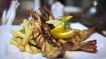 Prato com lagosta grelhada, fatias de limão e batatas fritas.